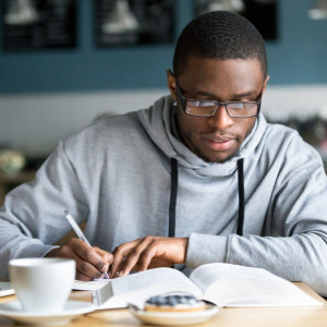 A Black student makes notes in a notebook while having coffee in a cafe