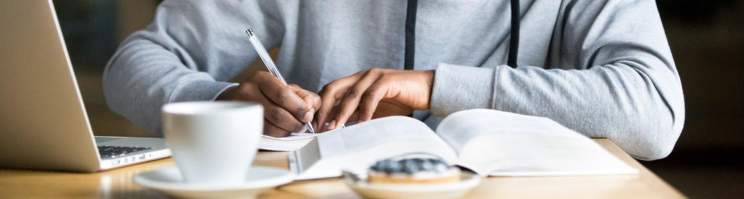A Black student makes notes in a notebook while having coffee in a cafe