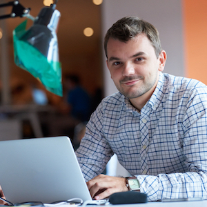 Smiling male student in plaid shirt working on computer in office space_300x300