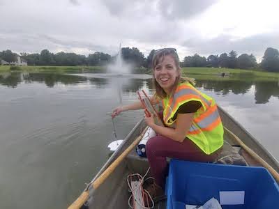 Kristin Seaman sits in a boat and tests the water in the middle of a pond