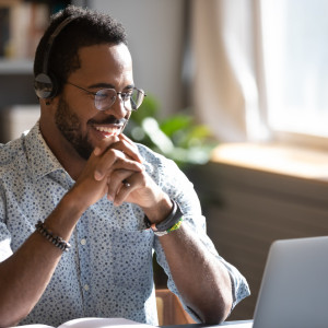 A man wearing headphones grins during an online meeting