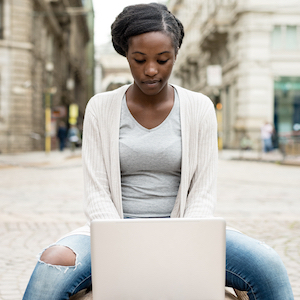 Young woman sitting on a bench and using a laptop computer in an urban setting