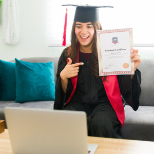 a young woman holds up her diploma to a laptop camera