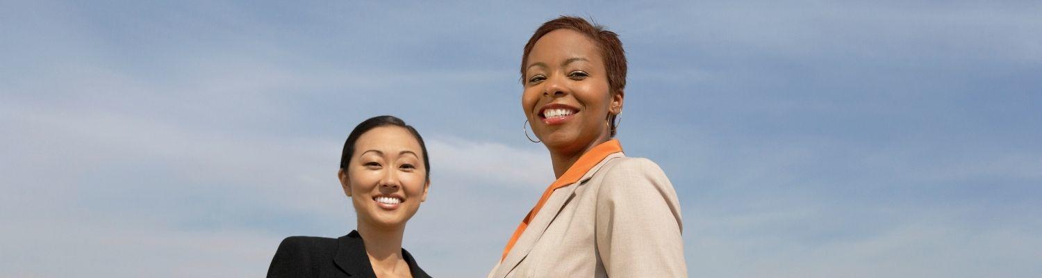 two business women standing outdoors with blue sky in background