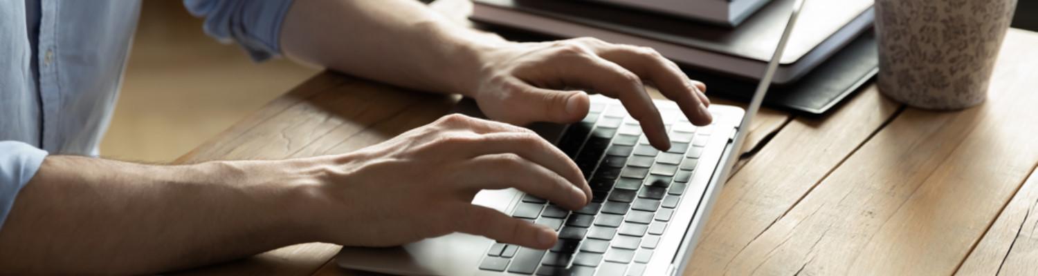 close-up of a man's hands typing on a laptop keyboard