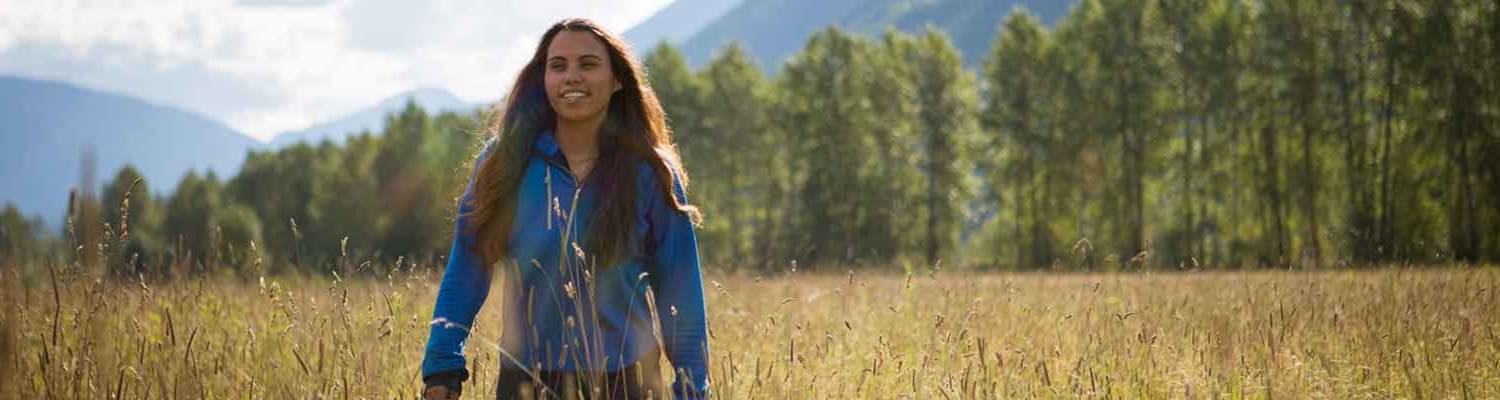 Indigenous Canadian woman walks toward the camera in a field of wheat on a sunny day