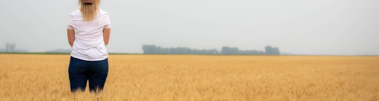A woman in T-shirt and jeans stands in a vast field of wheat