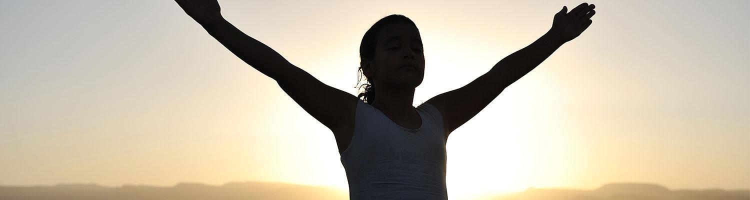 Woman holding out her arms with eyes closed in front of sun