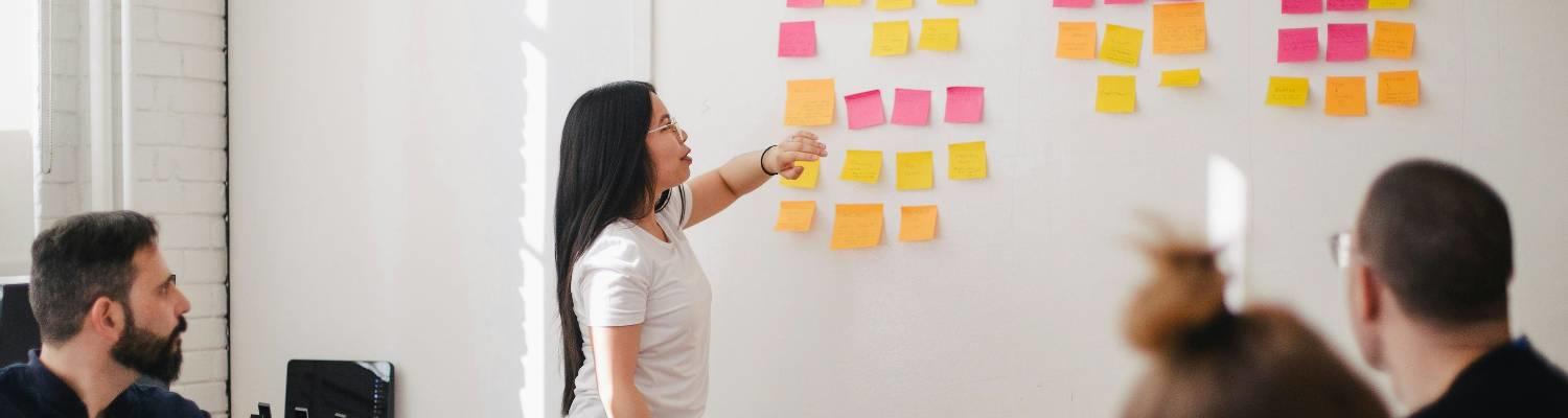 A woman discusses a plan outlined in sticky notes to her peers